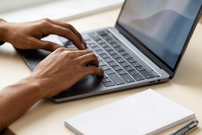Hände bei der Eingabe von Kontaktdaten auf einem Laptop neben einem Notizblock